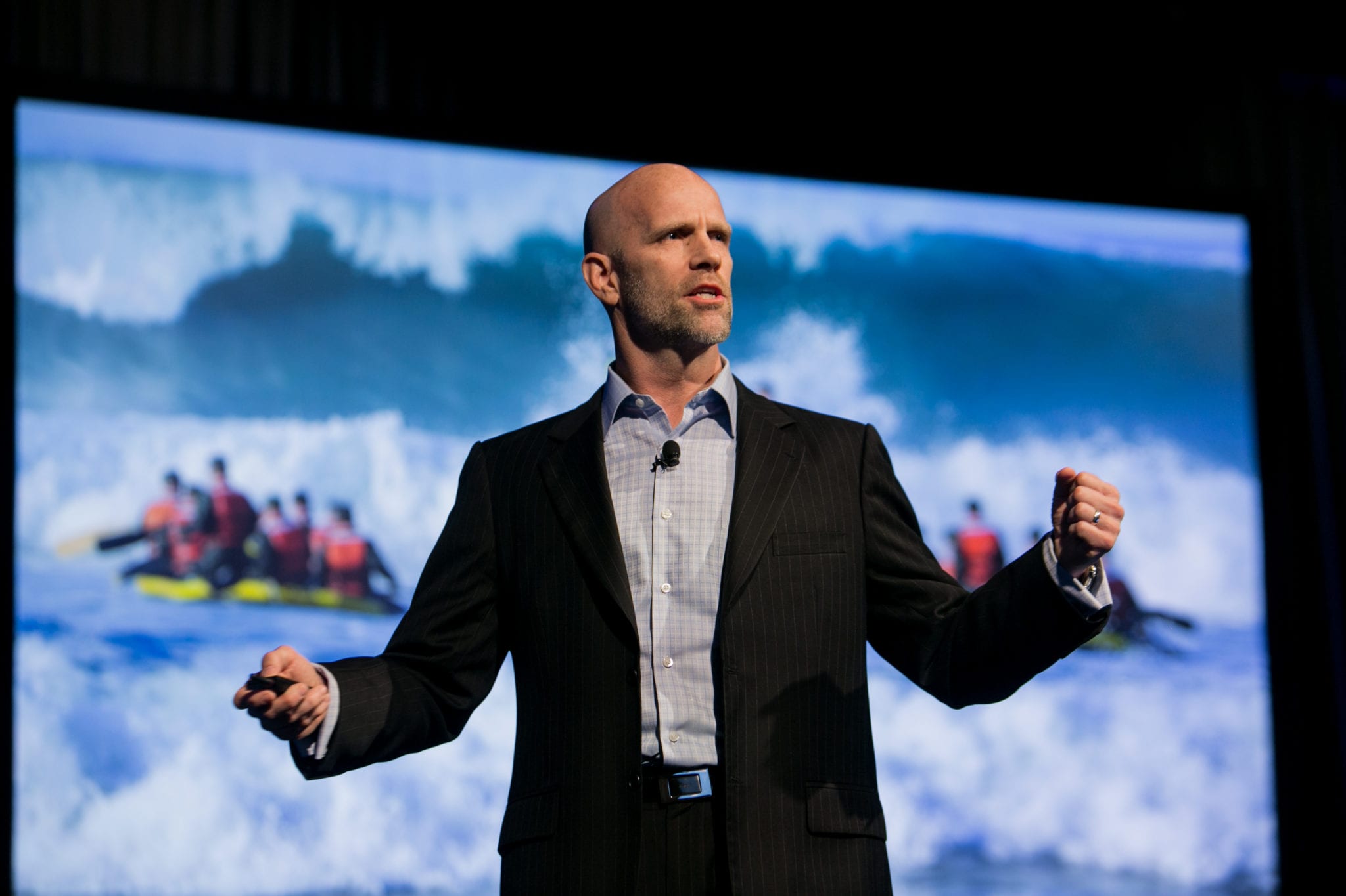 Navy SEAL Leadership Expert Errol Doebler standing on stage in front of screen showing people white water rafting
