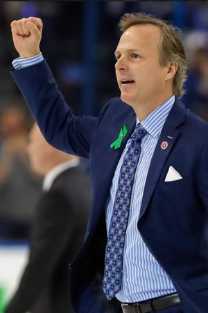 NHL Coach Jon Cooper in a black racket and blue shirt with a fist raised up in the air.