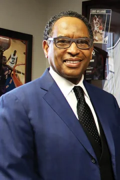 NBA Reggie Wilkes in a blue jacket and black tie, smiling.