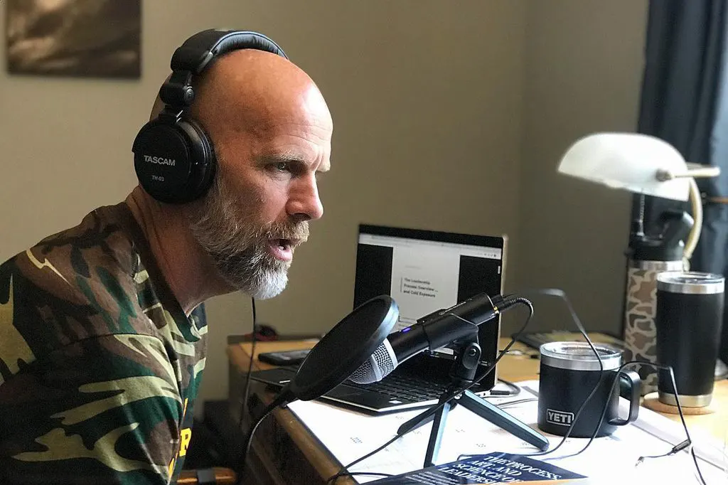 Former Navy SEAL Errol Doebler wearing a headset speaking into a microphone on his desk doing a keynote speaker podcast.