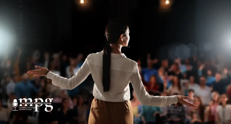 A motivational speaker with her arms stretched out in front of a crowd.