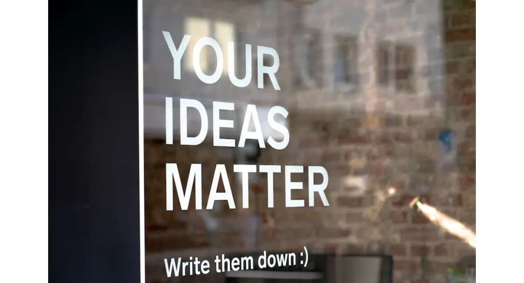A sign on glass reads motivational message, Your Ideas Matter, Write them down :)