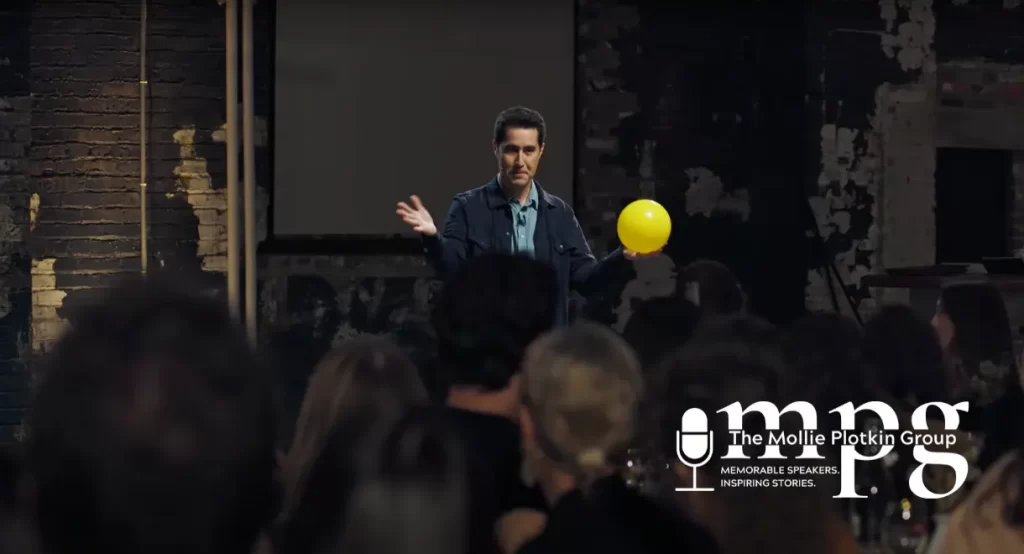 Magician David Kwong standing in front of a crowd, holding a yellow balloon.