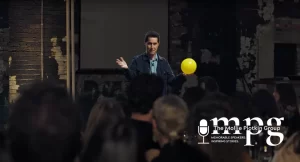 Magician David Kwong standing in front of a crowd, holding a yellow balloon.