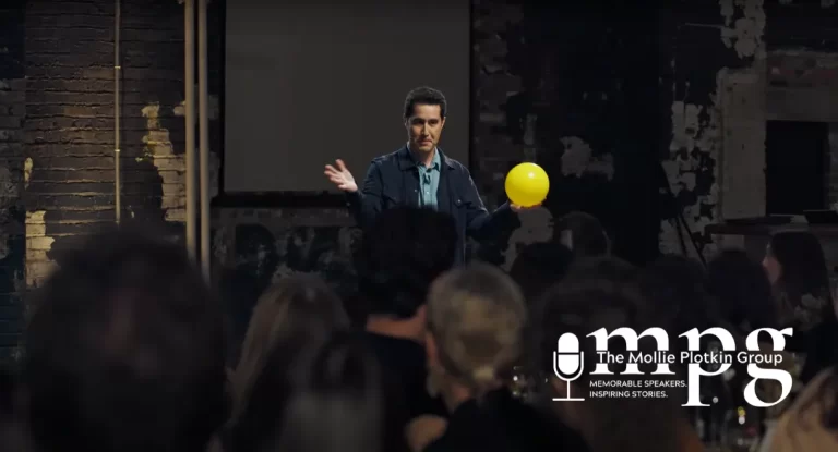 Magician David Kwong standing in front of a crowd, holding a yellow balloon.