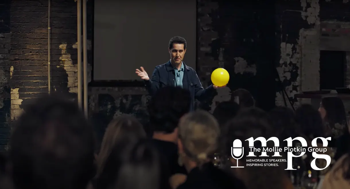 Magician David Kwong standing in front of a crowd, holding a yellow balloon.
